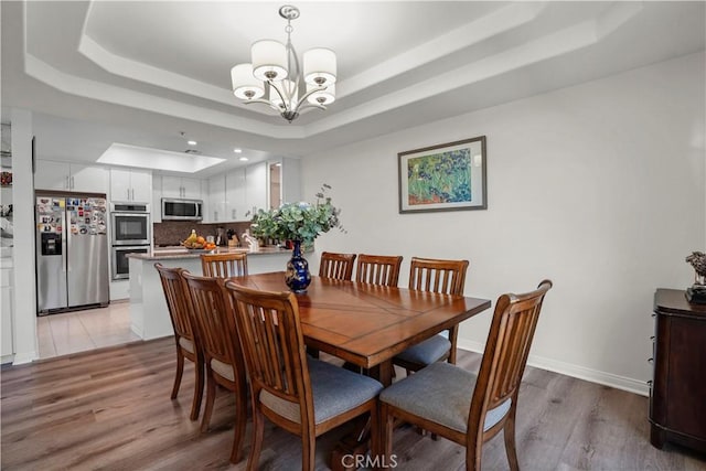 dining room featuring a tray ceiling, a chandelier, and light hardwood / wood-style flooring