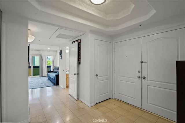 corridor with light tile patterned flooring and a tray ceiling