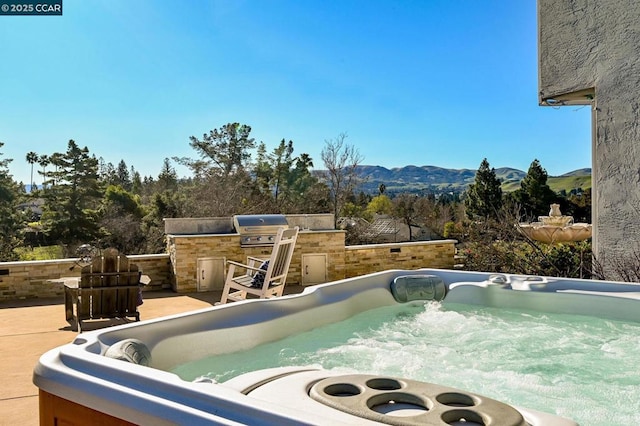 exterior space featuring a hot tub, a mountain view, an outdoor kitchen, and grilling area