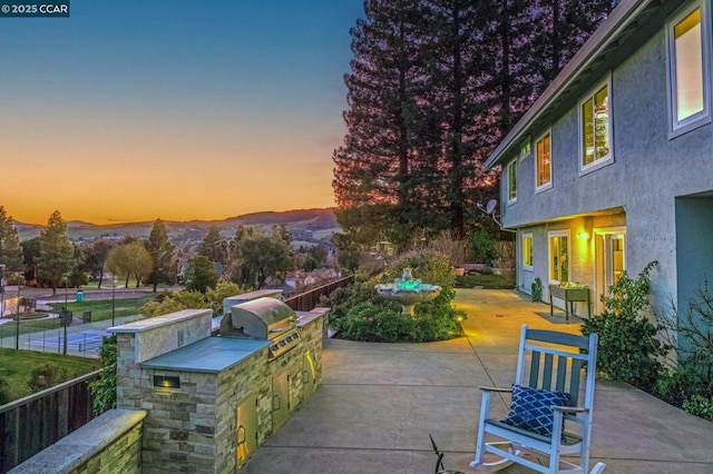 patio terrace at dusk with grilling area, exterior kitchen, and a mountain view