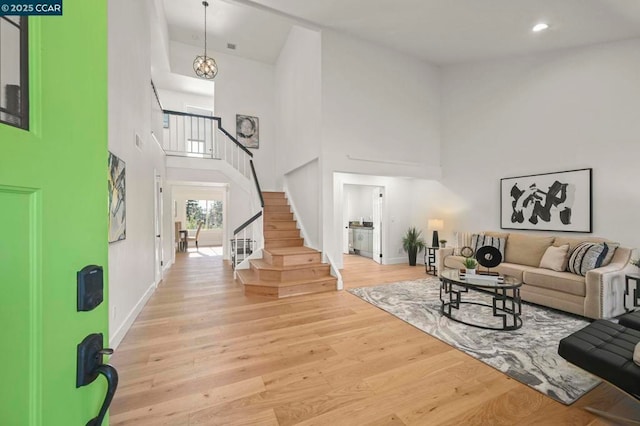 foyer entrance with an inviting chandelier, a towering ceiling, and light wood-type flooring