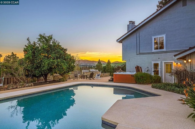 pool at dusk featuring a hot tub and a patio area