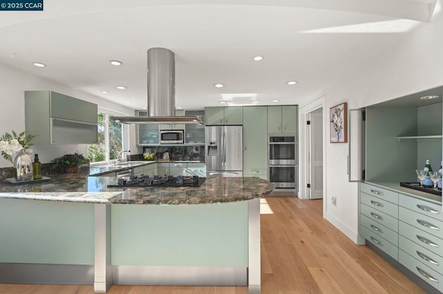 kitchen featuring dark stone countertops, kitchen peninsula, green cabinets, island exhaust hood, and stainless steel appliances