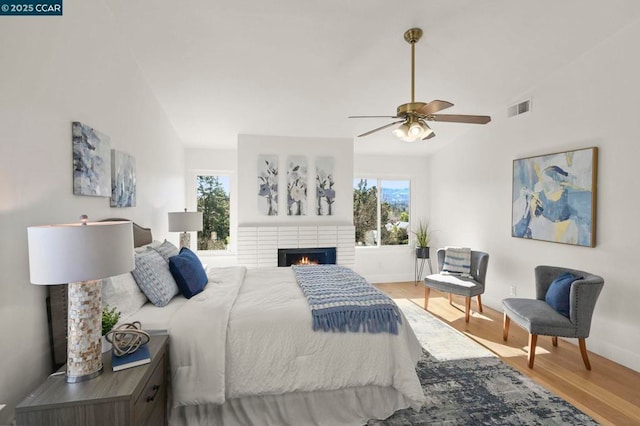 bedroom featuring vaulted ceiling, ceiling fan, hardwood / wood-style floors, and a brick fireplace