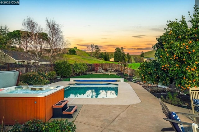 pool at dusk with a patio area and a hot tub