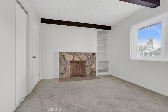 unfurnished living room with light carpet, a stone fireplace, and built in shelves