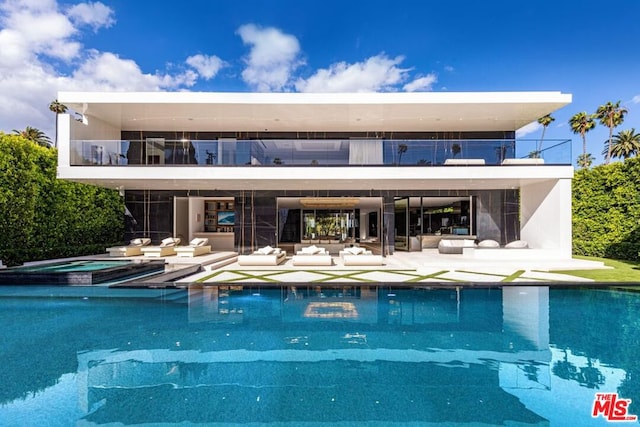 rear view of house with a pool with hot tub, a patio, and a balcony