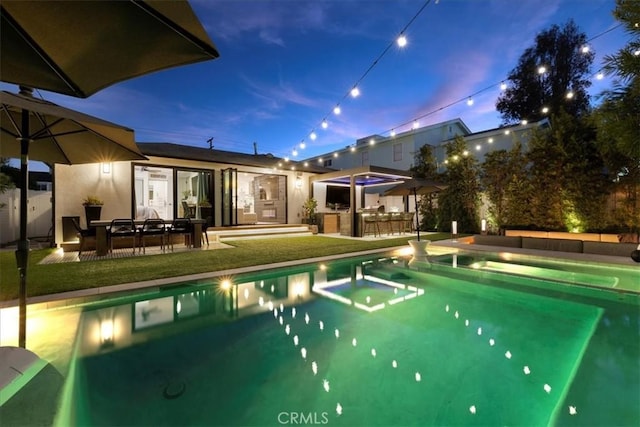 pool at dusk featuring a patio, an outdoor bar, and a yard