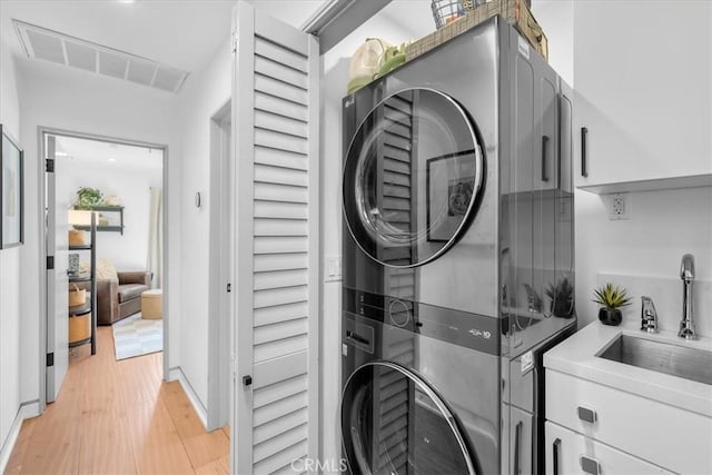 laundry room with sink, stacked washer and clothes dryer, and light hardwood / wood-style flooring