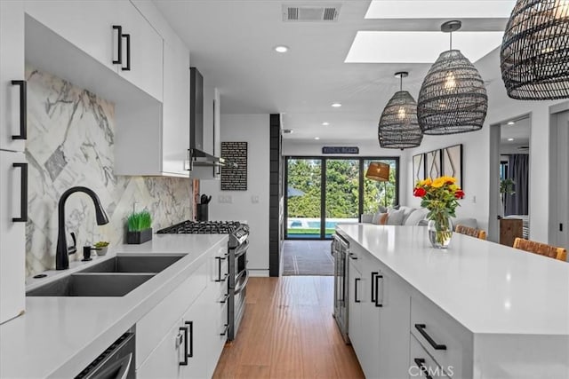 kitchen with appliances with stainless steel finishes, white cabinetry, decorative backsplash, sink, and pendant lighting