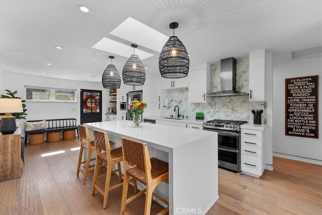 kitchen with wall chimney exhaust hood, a kitchen bar, decorative light fixtures, double oven range, and sink