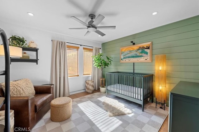 bedroom featuring ceiling fan, a nursery area, and wood walls