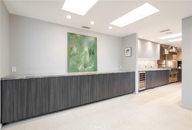 kitchen featuring white cabinetry, wall chimney range hood, beverage cooler, range with two ovens, and backsplash