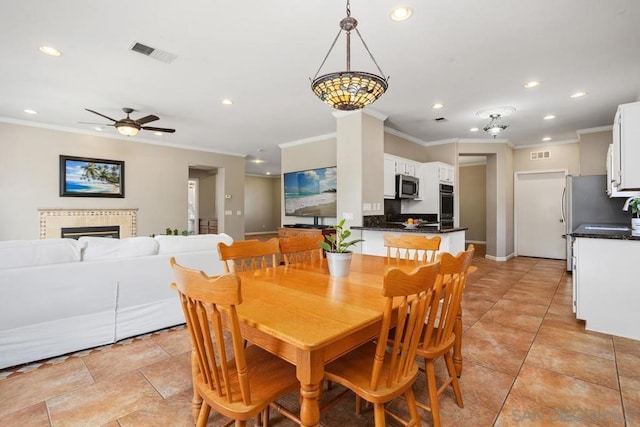 dining area with crown molding, ceiling fan, and a tile fireplace