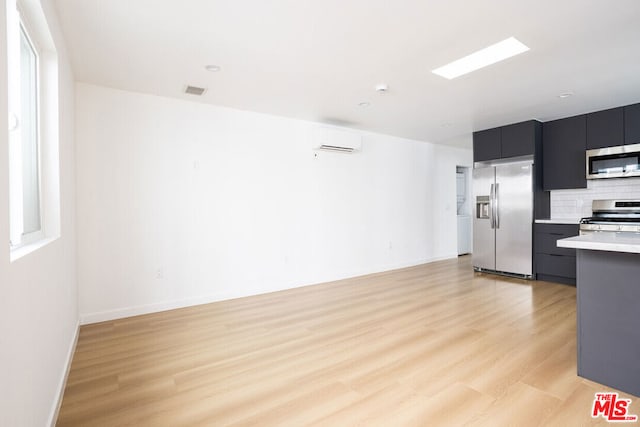 kitchen featuring light wood-type flooring, backsplash, a wall mounted AC, and appliances with stainless steel finishes