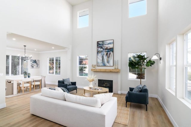 living room with crown molding, light wood-type flooring, a high ceiling, and a notable chandelier