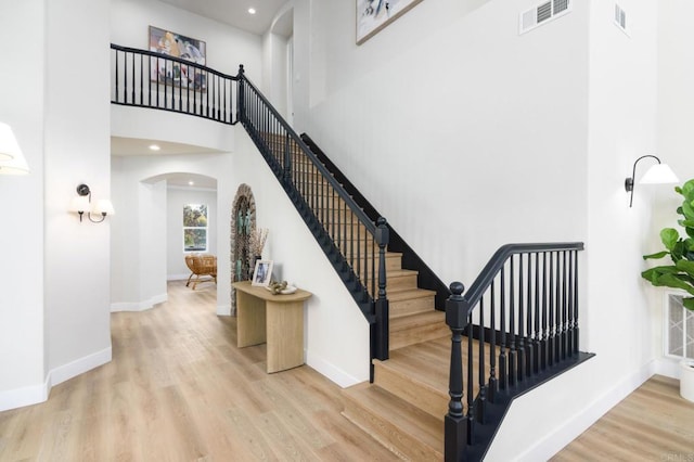 staircase with wood-type flooring and a towering ceiling