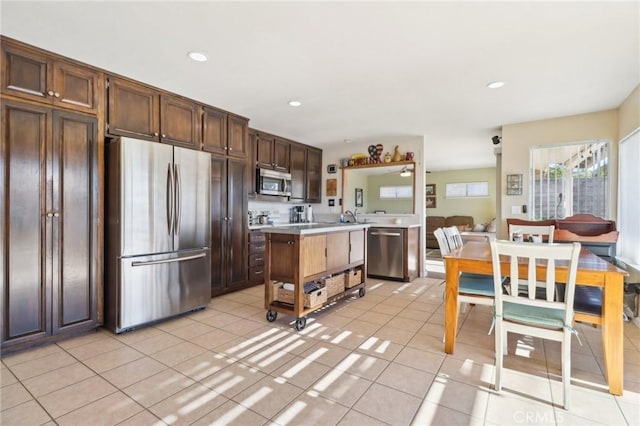 kitchen with light tile patterned floors, sink, appliances with stainless steel finishes, dark brown cabinets, and a kitchen island