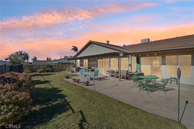 back house at dusk featuring a yard and a patio area