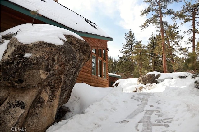 view of snowy exterior with a garage and log veneer siding