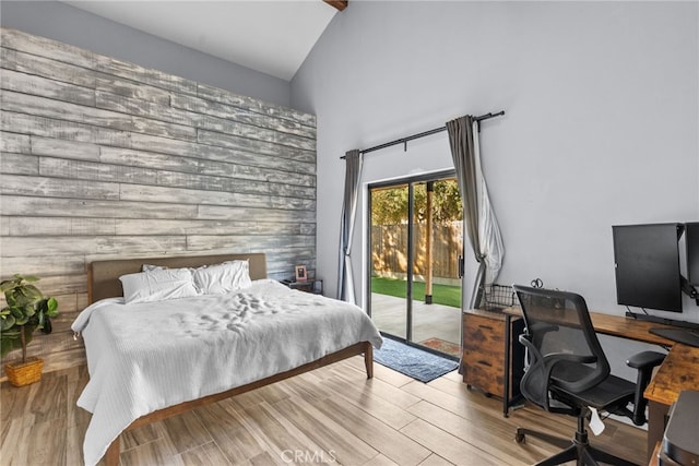 bedroom with access to exterior, light hardwood / wood-style flooring, lofted ceiling, and wooden walls