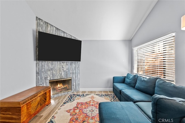 living room featuring wood-type flooring, a tiled fireplace, and lofted ceiling