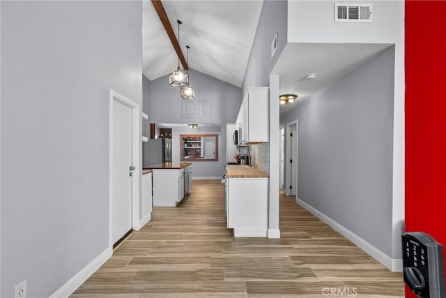 kitchen featuring decorative light fixtures, backsplash, lofted ceiling with beams, white cabinetry, and stainless steel appliances