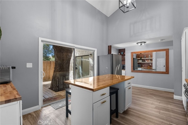 kitchen with wooden counters, white cabinets, light wood-type flooring, high vaulted ceiling, and stainless steel fridge