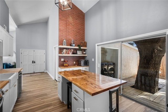 kitchen featuring white cabinetry, butcher block countertops, washing machine and clothes dryer, high vaulted ceiling, and light hardwood / wood-style floors