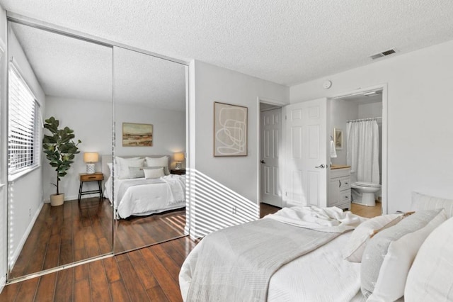 bedroom featuring ensuite bathroom, dark hardwood / wood-style flooring, and a textured ceiling