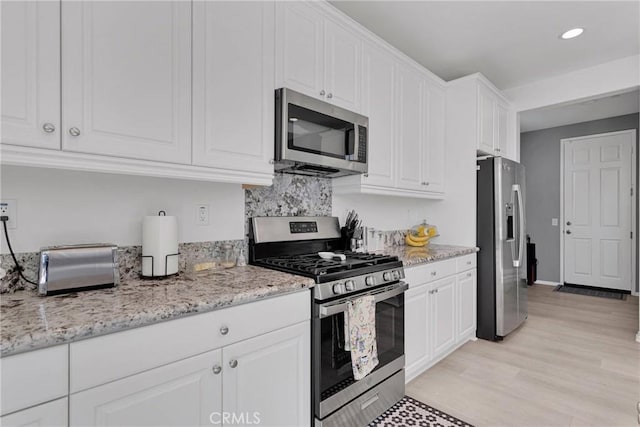 kitchen featuring white cabinets, light hardwood / wood-style floors, light stone countertops, and stainless steel appliances