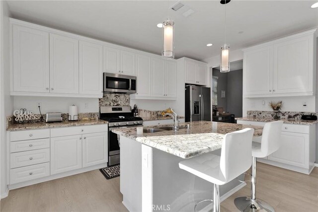 kitchen with stainless steel appliances, white cabinetry, light stone counters, and a kitchen island with sink