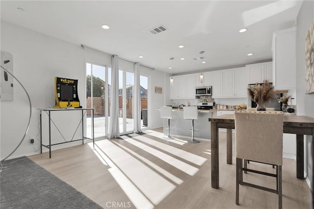 interior space with light hardwood / wood-style floors, white cabinetry, a kitchen island, a breakfast bar, and stainless steel appliances