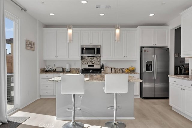 kitchen with light stone counters, a kitchen island with sink, hanging light fixtures, and stainless steel appliances