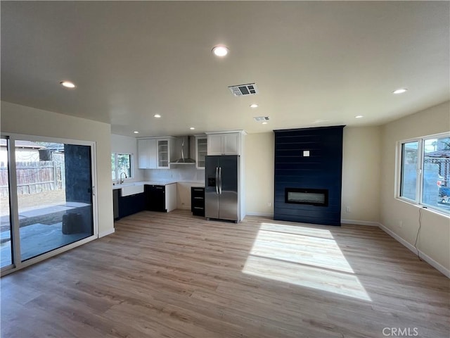 kitchen featuring wall chimney range hood, a wealth of natural light, light hardwood / wood-style floors, white cabinets, and stainless steel fridge with ice dispenser