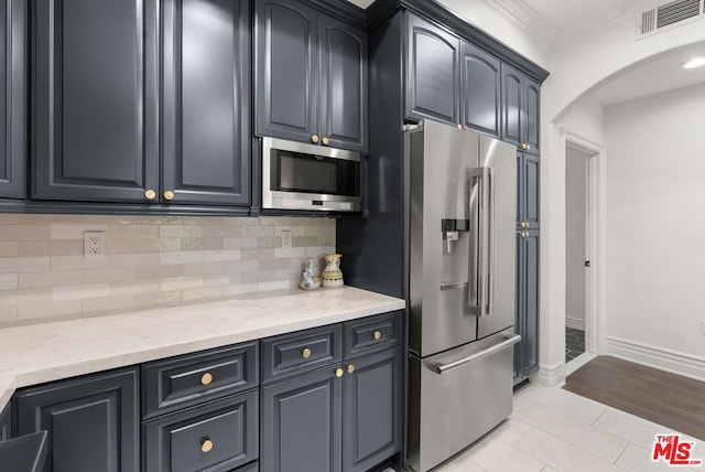 kitchen featuring appliances with stainless steel finishes, ornamental molding, backsplash, light stone counters, and light tile patterned flooring