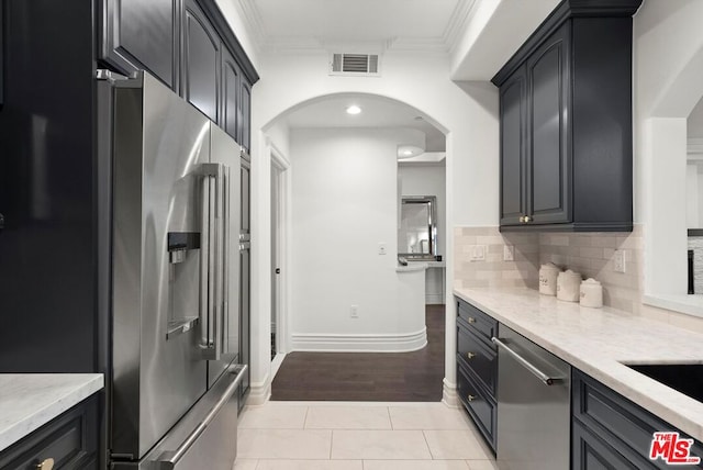 kitchen featuring light stone countertops, appliances with stainless steel finishes, decorative backsplash, ornamental molding, and light tile patterned floors