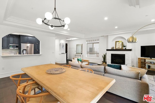 dining space with crown molding, a raised ceiling, a stone fireplace, dark hardwood / wood-style floors, and a notable chandelier