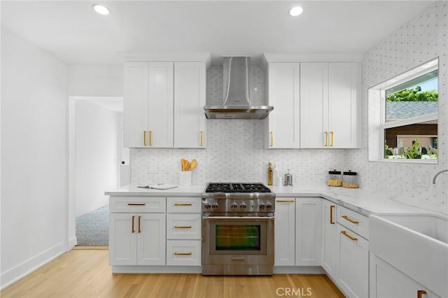 kitchen with wall chimney range hood, white cabinetry, stainless steel range, and sink