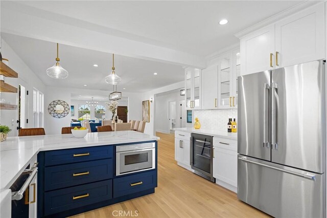 kitchen with hanging light fixtures, white cabinets, blue cabinetry, beverage cooler, and stainless steel appliances