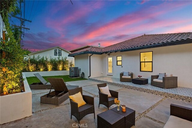 back house at dusk featuring central air condition unit, outdoor lounge area, and a patio