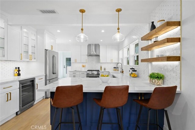 kitchen featuring wine cooler, high end appliances, white cabinets, wall chimney exhaust hood, and a breakfast bar area