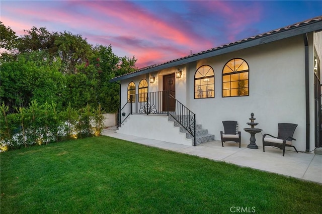 back house at dusk with a yard and a patio