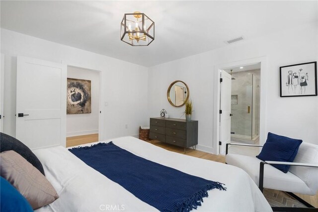 bedroom with light wood-type flooring, a chandelier, and ensuite bath