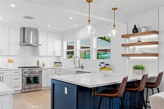 kitchen with wall chimney exhaust hood, white cabinetry, light stone countertops, a breakfast bar, and high end range