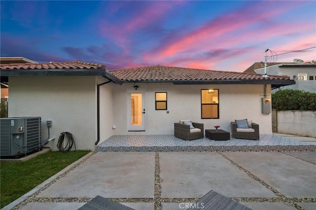 back house at dusk featuring outdoor lounge area, a patio, and central air condition unit