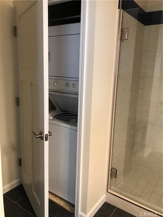 clothes washing area featuring dark tile patterned flooring and stacked washer and clothes dryer