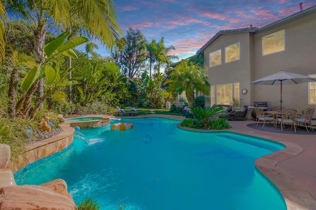 pool at dusk with an in ground hot tub and a patio