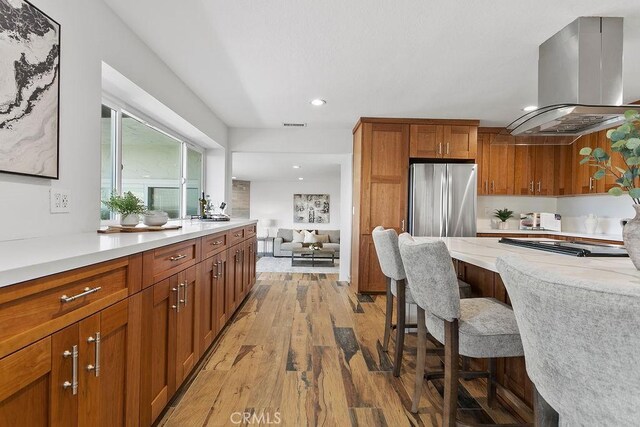 kitchen with island range hood, stainless steel refrigerator, a kitchen breakfast bar, black electric stovetop, and light hardwood / wood-style flooring