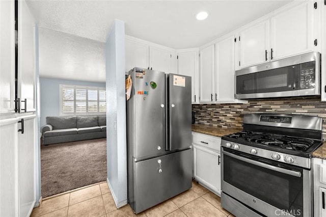 kitchen featuring white cabinetry, stainless steel appliances, light carpet, decorative backsplash, and dark stone counters